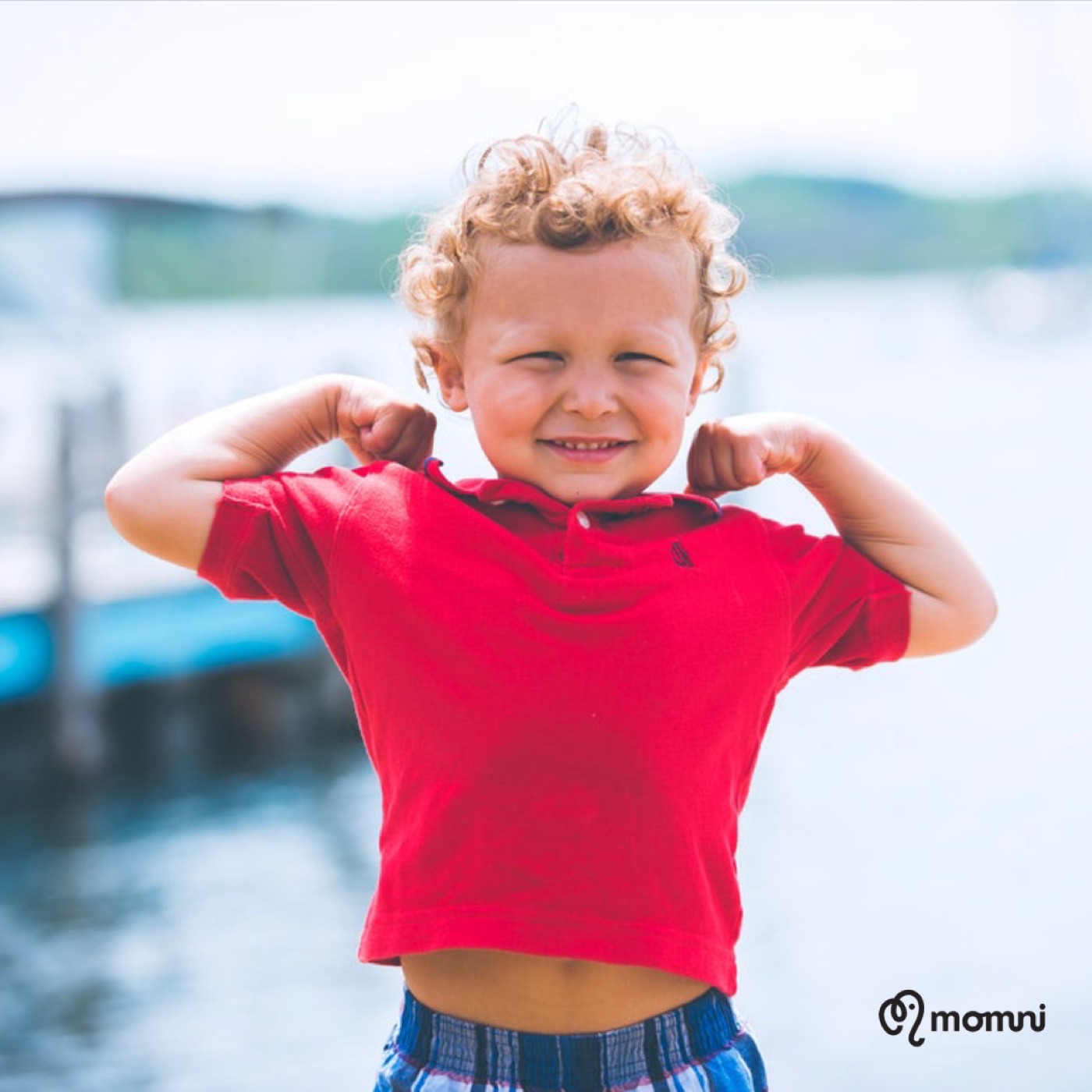 A curly-haired boy flexing his little muscles by the lake, all grins
