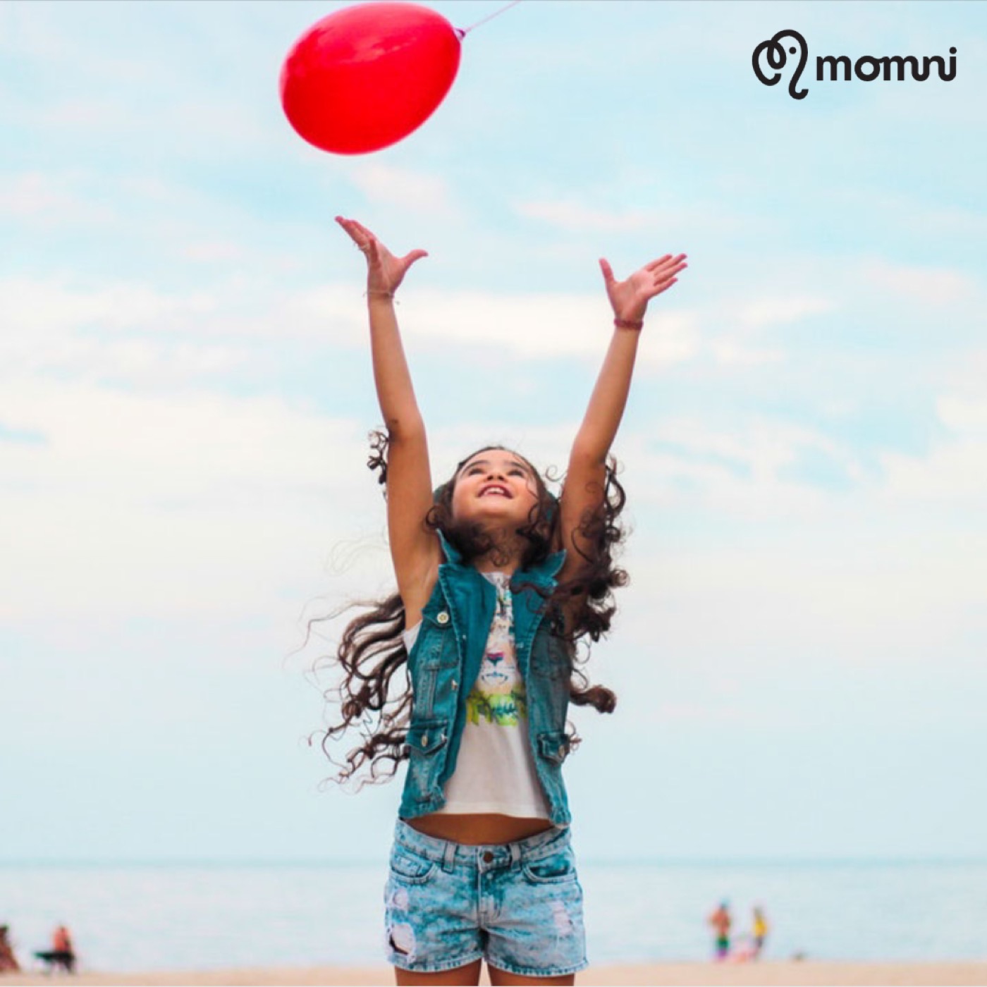 A little girl tossing a red balloon into the beach sky