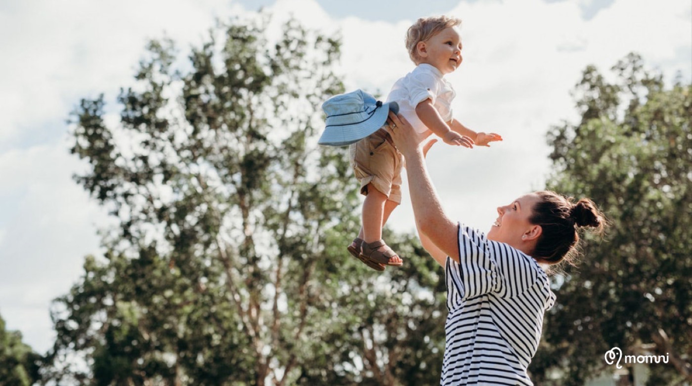 A mama lifting her giggling toddler toward the sky